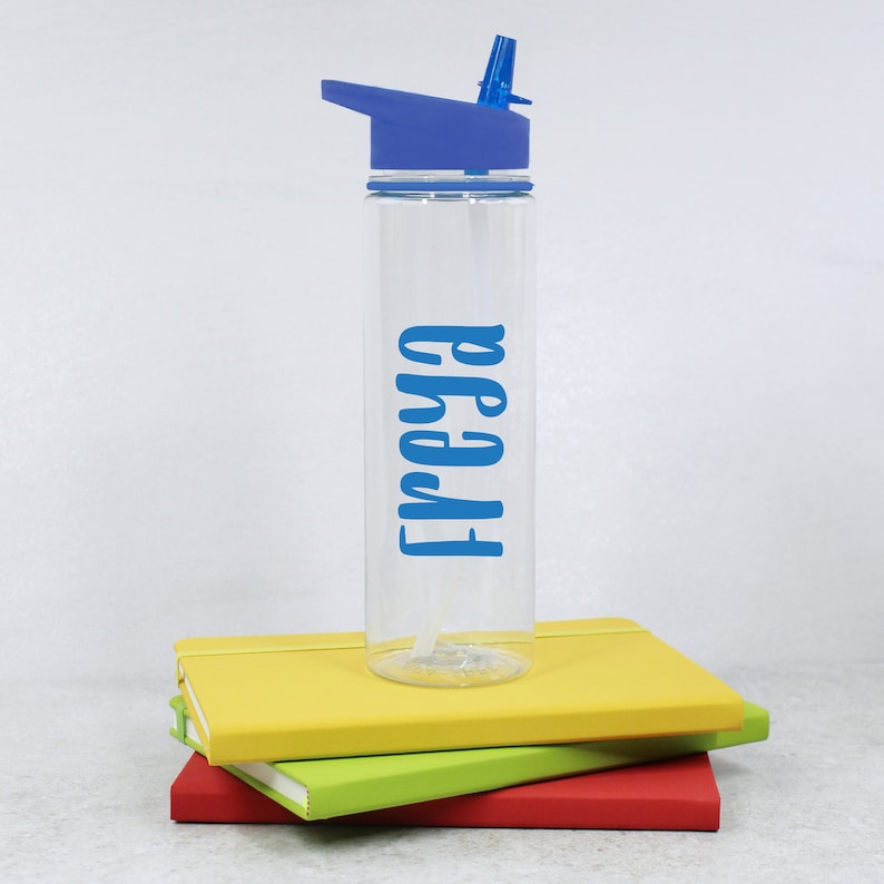 May include: A clear plastic water bottle with a blue lid and a blue straw. The bottle has the name "Freya" written on it in blue lettering.
