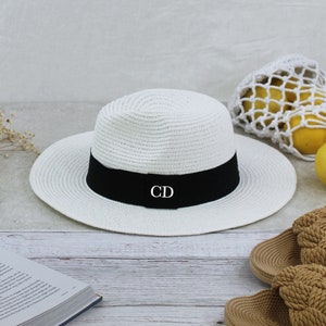 Peut inclure: Chapeau de paille blanc avec un ruban noir et les initiales "CD" brod&eacute;es sur le ruban.