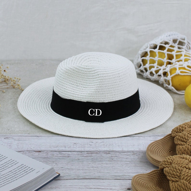 Peut inclure: Chapeau de paille blanc avec un ruban noir et les initiales "CD" brod&eacute;es sur le ruban.