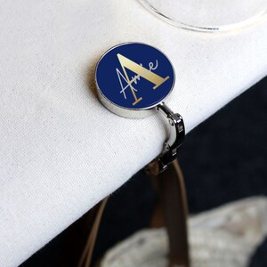May include: A silver-toned table clip with a round blue base and a gold letter "A" with the name "Anne" written in gold script.