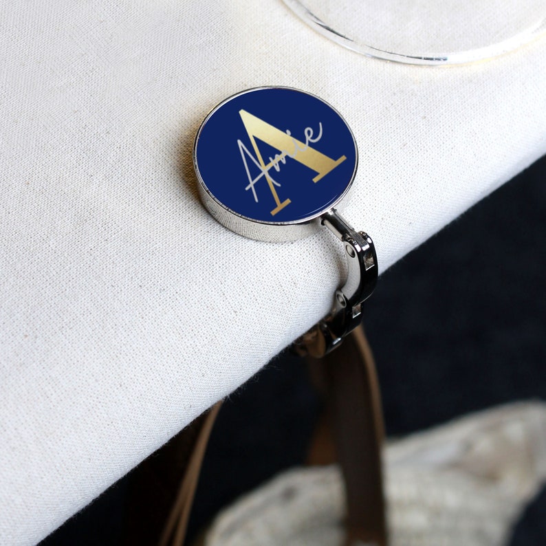 May include: A silver-toned table clip with a round blue base and a gold letter "A" with the name "Anne" written in gold script.