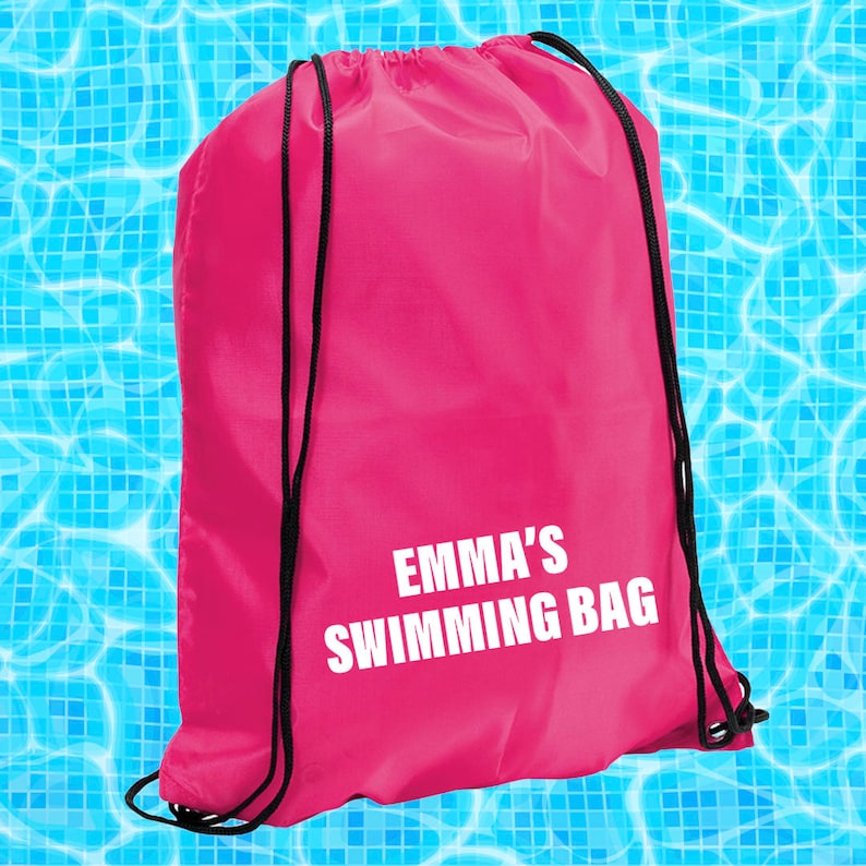 May include: A pink drawstring bag with black drawstrings. The bag has white text that says "EMMA'S SWIMMING BAG".