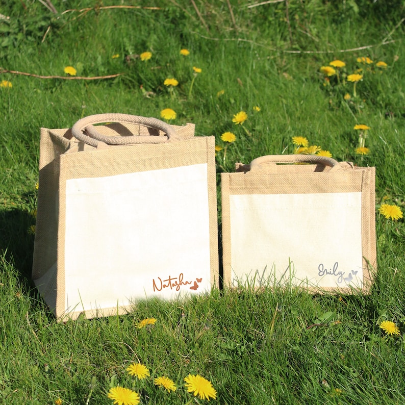 May include: Two natural jute tote bags with white fabric panels. The larger bag has the name "Natasha" written in brown script with two small hearts. The smaller bag has the name "Emily" written in grey script with two small hearts.