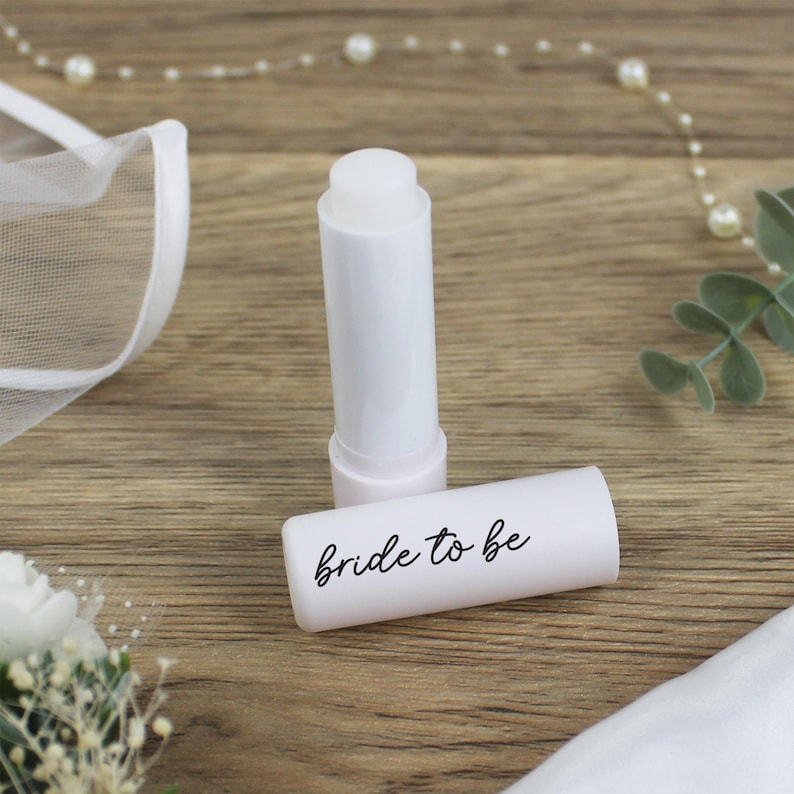 K&ouml;nnte beinhalten: Wei&szlig;er Lippenbalsam-Stift mit einem wei&szlig;en Etikett, auf dem in schwarzer Schrift "bride to be" steht.