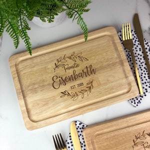 May include: A wooden cutting board with a personalized inscription that reads "Familie Eisenbarth EST. 2009" with a decorative floral wreath around the text.