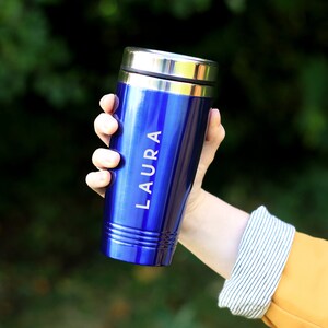 May include: A blue stainless steel travel mug with a silver lid and the name "LAURA" engraved on the side.