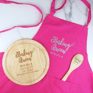 May include: A pink apron with a silver glitter "Baking Queen" inscription and a wooden cutting board with the same inscription, but with the name "Nicola" and the text "Speciality: Top Class Chocolate Sponge".