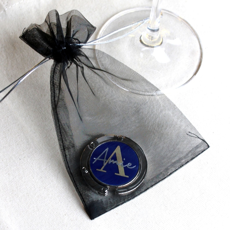 May include: A black mesh bag with a silver and blue personalized purse hook with the name "Amie" on it.