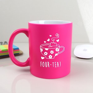 May include: A bright pink ceramic mug with a white design of a teacup with a teabag and the text "FOUR-TEA!"