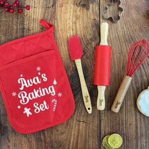 Könnte beinhalten: Ein rotes Backset mit dem Text "Ava's Baking Set" auf einem roten Topflappen. Enthält einen roten Spatel, eine Teigrolle und einen Schneebesen, alle mit Holzgriffen. Enthält auch Ausstecher, Kekse und Süßigkeiten.