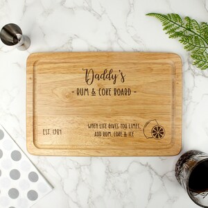 May include: A wooden cutting board with the text "Daddy's - RUM & COKE BOARD - EST. 1984" and the phrase "WHEN LIFE GIVES YOU LIMES, ADD RUM, COKE & ICE" with a lemon illustration.