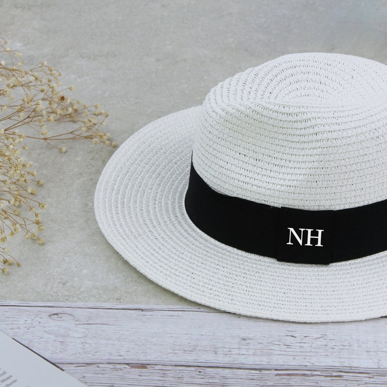 Peut inclure: Chapeau de paille blanc avec un ruban noir et les initiales "NH" brod&eacute;es sur le ruban.