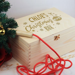 Peut inclure: Une boîte en bois avec une corde rouge attachée au couvercle. La boîte est décorée du texte "CHLOE'S Christmas Eve BOX" en lettres dorées.