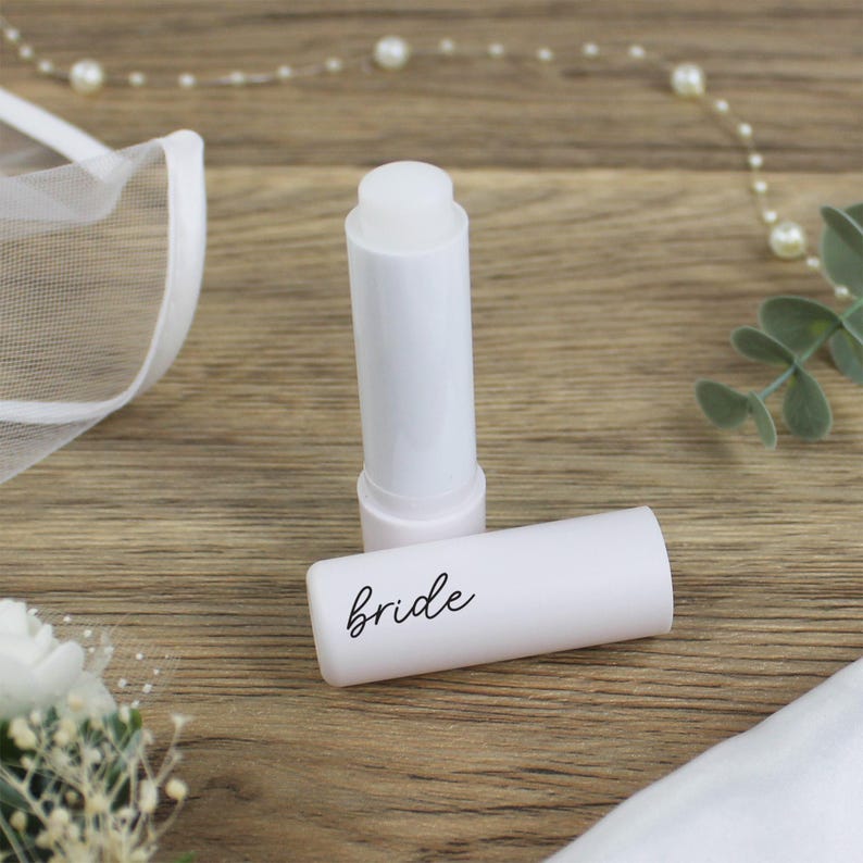 K&ouml;nnte beinhalten: Wei&szlig;er Lippenbalsam-Stift mit dem Wort "bride" auf der Seite. Der Stift liegt auf einer Holzoberfl&auml;che.