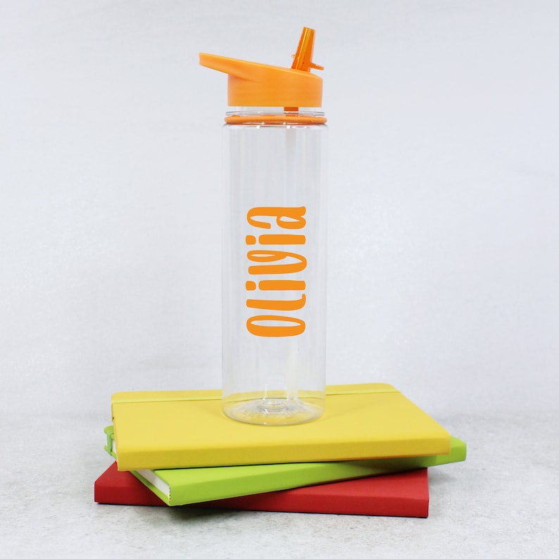 May include: Orange and clear plastic water bottle with a flip top lid and straw. The bottle has the name "Olivia" printed on it in orange.
