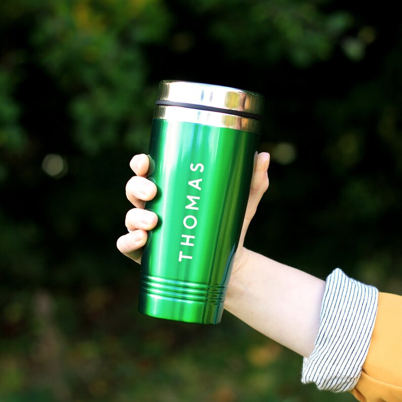 May include: A green travel mug with a silver lid and the name "THOMAS" engraved on the side.