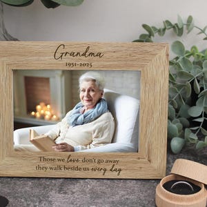 May include: A wooden photo frame with a picture of a woman and the text "Grandma 1951-2025" and "Those we love don't go away, they walk beside us every day".