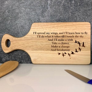 Może przedstawiać: Drewniana deska do krojenia z uchwytem, grawerowana z tekstem "I'll spread my wings, and I'll learn how to fly I'll do what it takes till I touch the sky And I'll make a wish Take a chance Make a change And breakaway" i stadem ptaków lecących w formacji V.