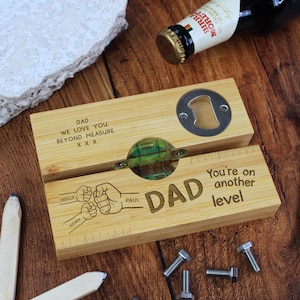 May include: A wooden bottle opener gift set with a built-in level and bottle opener. The set is engraved with the word "DAD", the text "You're on another level", and the names Holly, Paul, and Noah. A bottle of Birra Moretti beer is in the background.