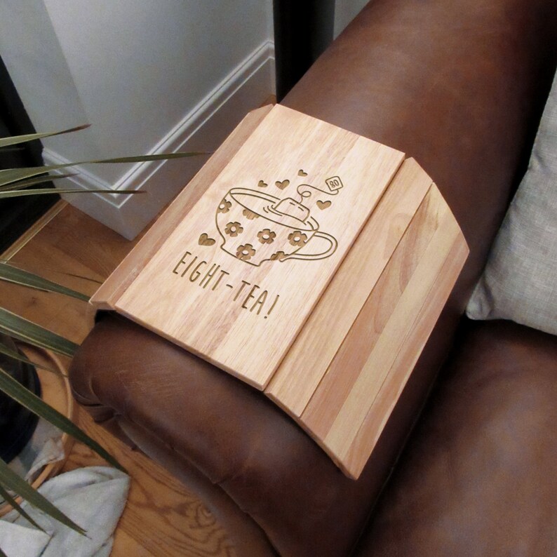 May include: Wooden tray with a cup and teabag design and the text "Eight-Tea!" engraved on it. The tray is designed to fit over the arm of a couch or chair.