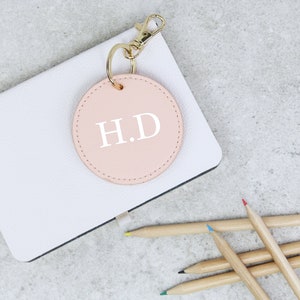 May include: A pink leather keychain with a gold key ring and a round charm with the initials "H.D." in white lettering.