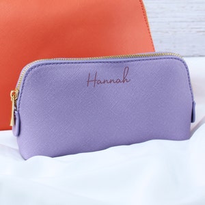 May include: A lavender-colored zippered pouch with a gold zipper and the name "Hannah" embossed in a cursive font.