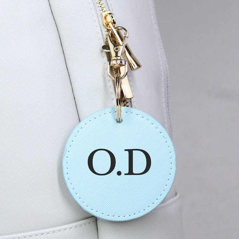 May include: A light blue round leather keychain with the initials "O.D." in black lettering.
