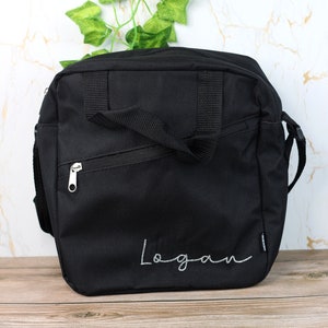Pode incluir: Uma bolsa de ombro de lona preta com um bolso com z&iacute;per e um puxador de z&iacute;per prateado. A bolsa tem uma al&ccedil;a ajust&aacute;vel preta e o nome "Logan" &eacute; bordado em branco na frente.