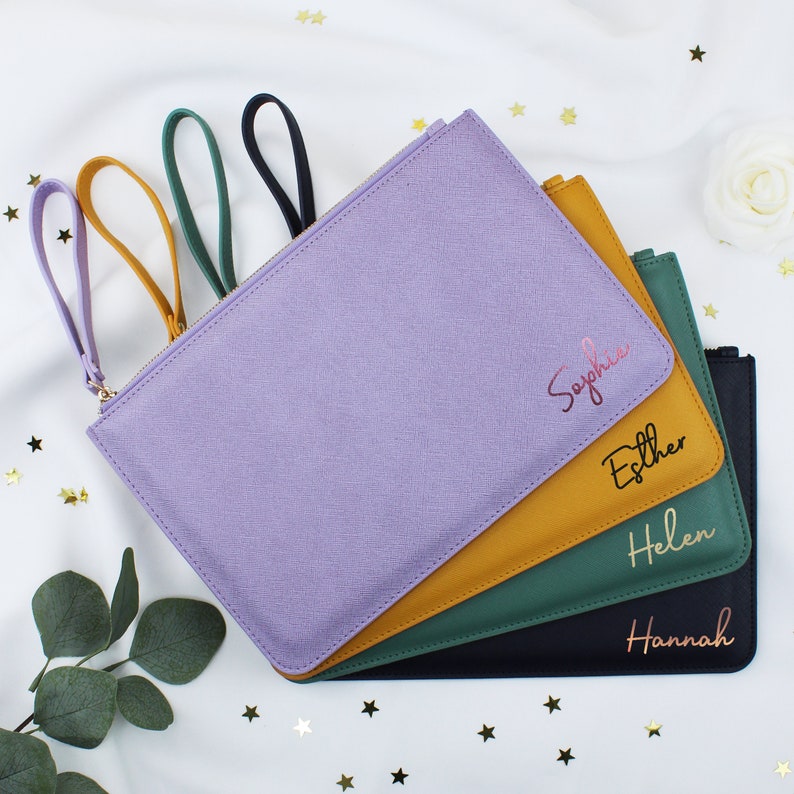 May include: Four personalised zippered pouches in different colours: lavender, mustard yellow, forest green, and black. The pouches have gold lettering with the names Sophia, Esther, Helen, and Hannah.