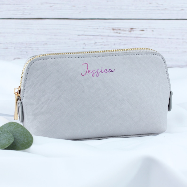 May include: A gray zippered cosmetic bag with a gold zipper and the name "Jessica" printed in pink on the front.