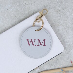 May include: A gray leather keychain with a gold metal ring and clasp. The keychain has a round, gray leather tag with the initials "W.M" in burgundy.