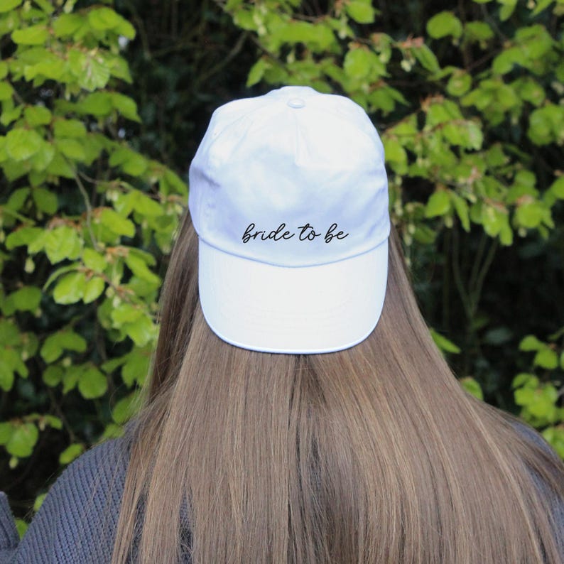 May include: White baseball cap with black embroidery that reads "bride to be".