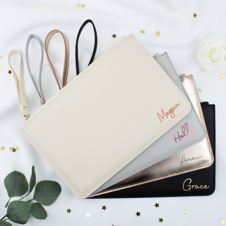 May include: Four personalised zippered pouches in different colours: cream, grey, gold, and black. Each pouch has a different name written in rose gold lettering: Megan, Holly, Annie, and Grace.