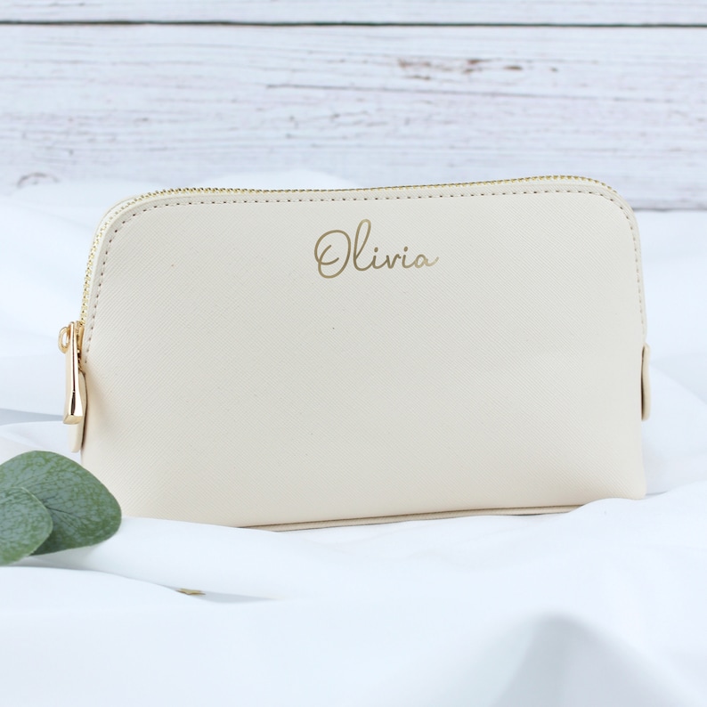 May include: A cream-colored zippered pouch with a gold zipper and the name "Olivia" written in gold script.