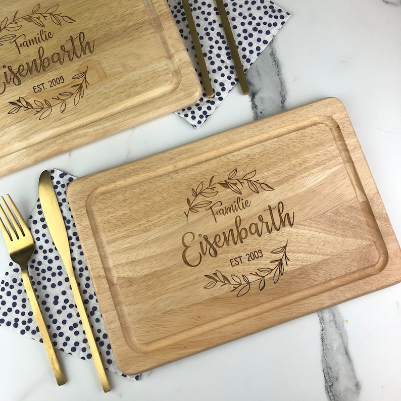 May include: Two wooden cutting boards with a natural wood finish. The boards are engraved with the text "Familie Eisenbarth EST. 2009" and a floral design.