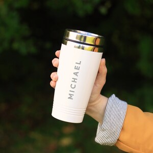 May include: White travel mug with a silver lid and the name "MICHAEL" printed on the side.
