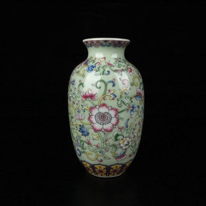 May include: A green ceramic vase with a floral pattern in shades of pink, blue, yellow, and green. The vase has a rounded body and a narrow neck.