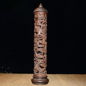 May include: A tall, intricately carved wooden incense holder. The dark brown cylinder features detailed relief carvings of clouds and swirling patterns. It has a rounded base and a conical top, showcasing a traditional design.
