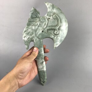 May include: A green jade axe with intricate carvings. The axe head is shaped like a bird with a long, thin handle.
