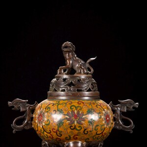 May include: Bronze incense burner with a yellow enamel body decorated with floral patterns in red, green, and white. The burner features dragon-shaped handles and a lion statue on the lid. The burner stands on three elephant-shaped legs.