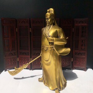 May include: A gold-colored statue of a Chinese deity holding a sword. The statue is standing on a wooden platform.
