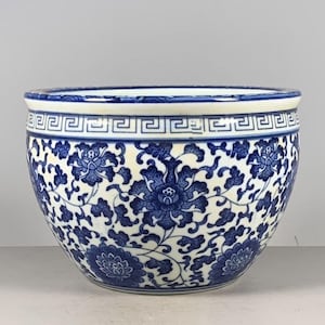 Könnte beinhalten: Eine runde, weiß-blaue Keramikschale mit floralem Design. Die Schale hat ein sich wiederholendes blaues Blumenmuster auf der Außenseite und einen geometrischen Rand um den Rand. Die Schale wird wahrscheinlich zu dekorativen Zwecken verwendet.