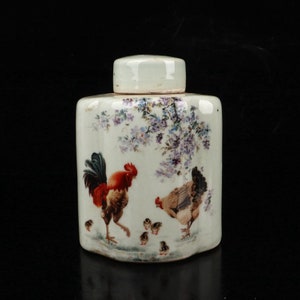 May include: A white ceramic jar with a lid, decorated with a rooster, hen, and chicks. The jar has a floral design with purple flowers and green leaves.