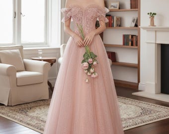Peut inclure: Une robe rose clair à épaules dénudées avec un corsage ajusté et une jupe fluide. La robe présente des détails de dentelle délicats sur le corsage et les manches. La personne tient un bouquet de roses roses. L'arrière-plan comprend une bibliothèque et une cheminée.