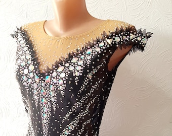 Può includere: Un body nero con scollatura a rete trasparente e maniche corte. Il body è decorato con strass iridescenti in un motivo geometrico.