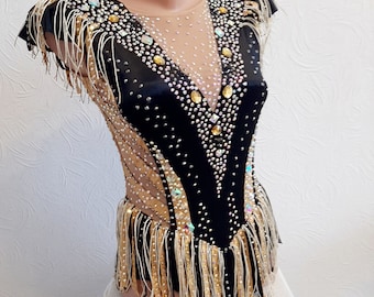 May include: A black and gold leotard with a sheer mesh bodice and fringe trim. The leotard is decorated with rhinestones and sequins.
