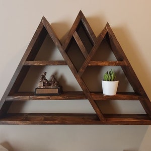 May include: A dark brown wooden mountain-shaped shelf with five shelves. The shelf is decorated with a small bronze statue and a potted succulent plant.