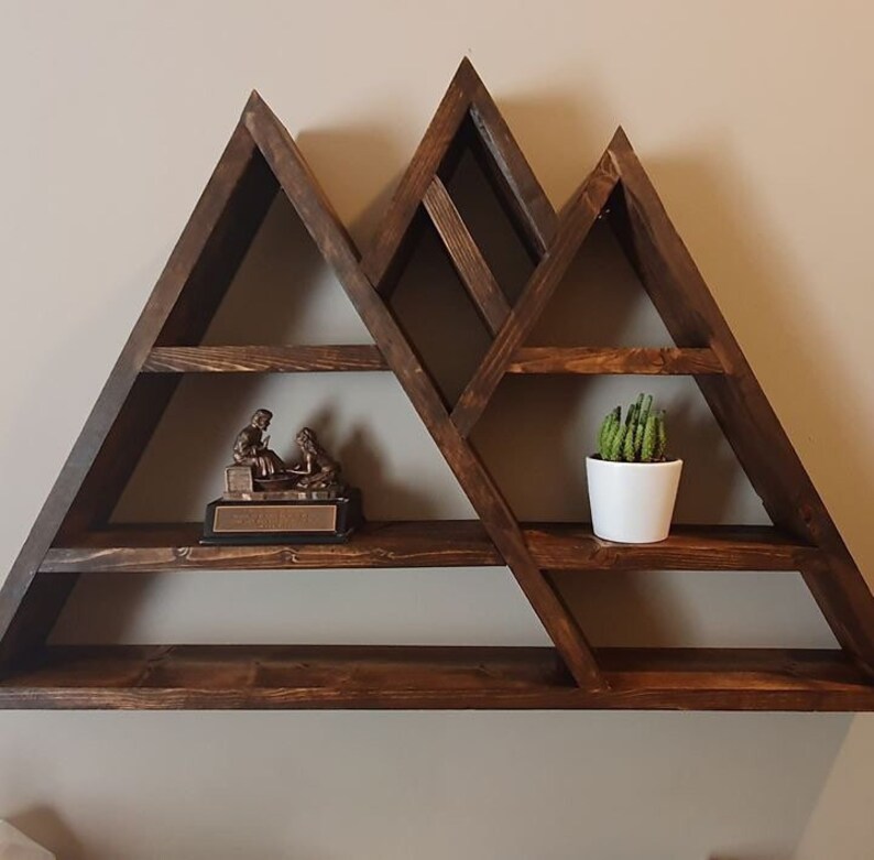 May include: A dark brown wooden mountain-shaped shelf with five shelves. The shelf is decorated with a small bronze statue and a potted succulent plant.