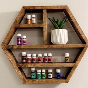 May include: A hexagonal wooden shelf with multiple shelves for displaying small bottles. The shelf is stained a dark brown colour and has a rustic look. There are several small bottles on the shelves, some with colourful liquids inside. A small potted plant sits on the top shelf.
