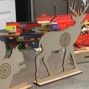May include: Two wooden target practice figures, a deer and a squirrel, with bullseye targets painted on them. The figures are painted white and are standing on wooden bases.